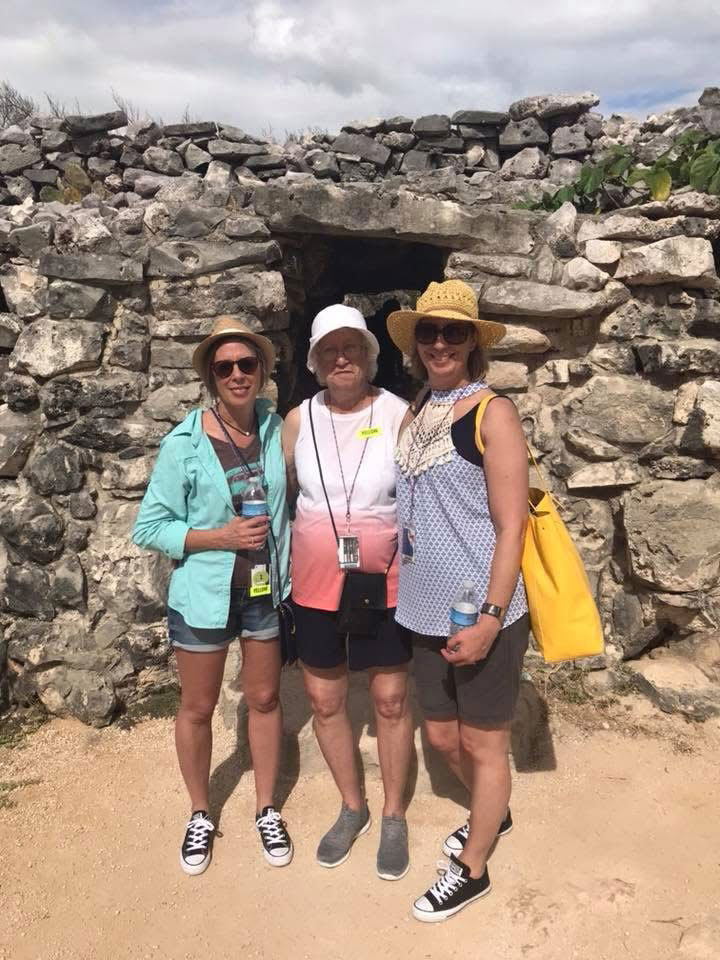 Dina Mason with her mother and sister smiling together in front of ancient stone ruins during a trip